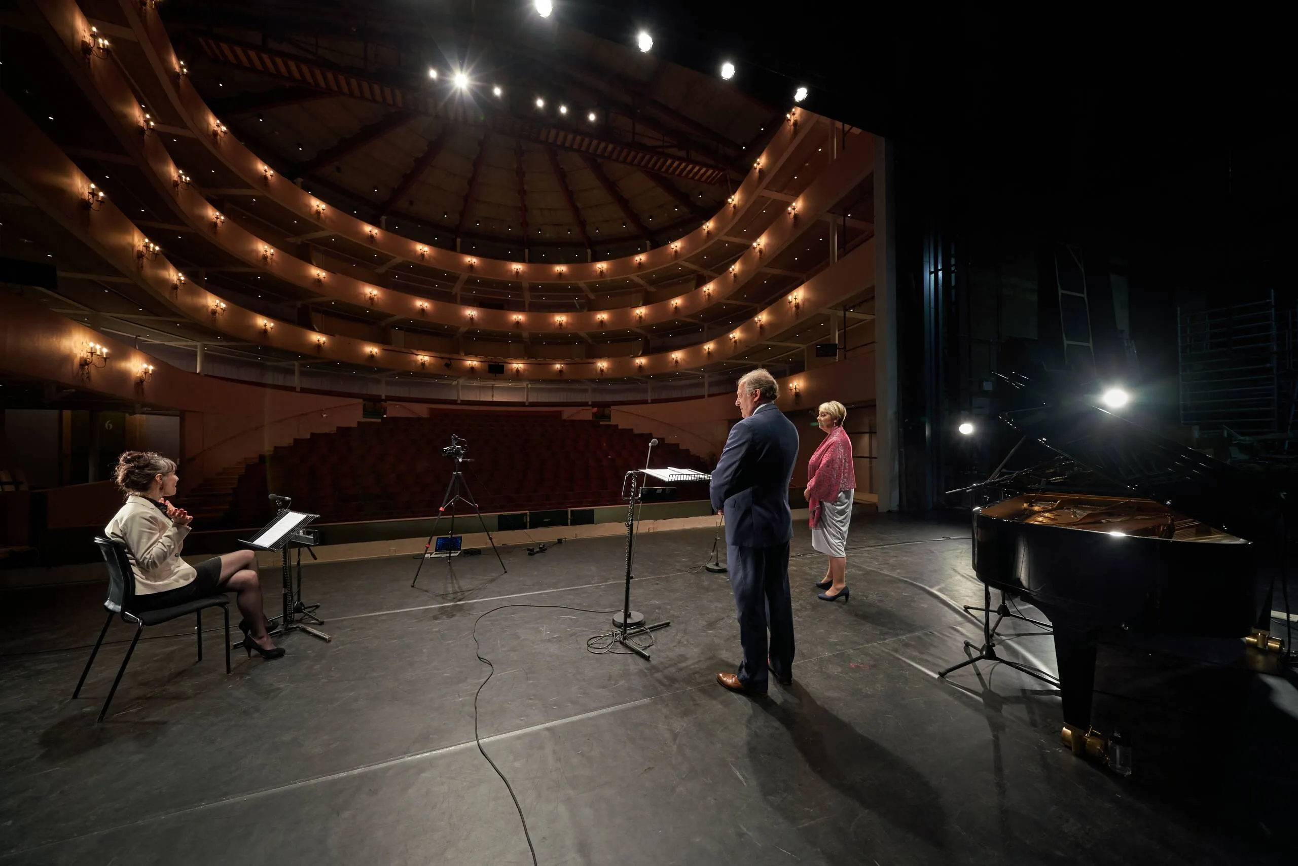 An empty horseshoe auditorium seen from the stage during a rehearsal with piano