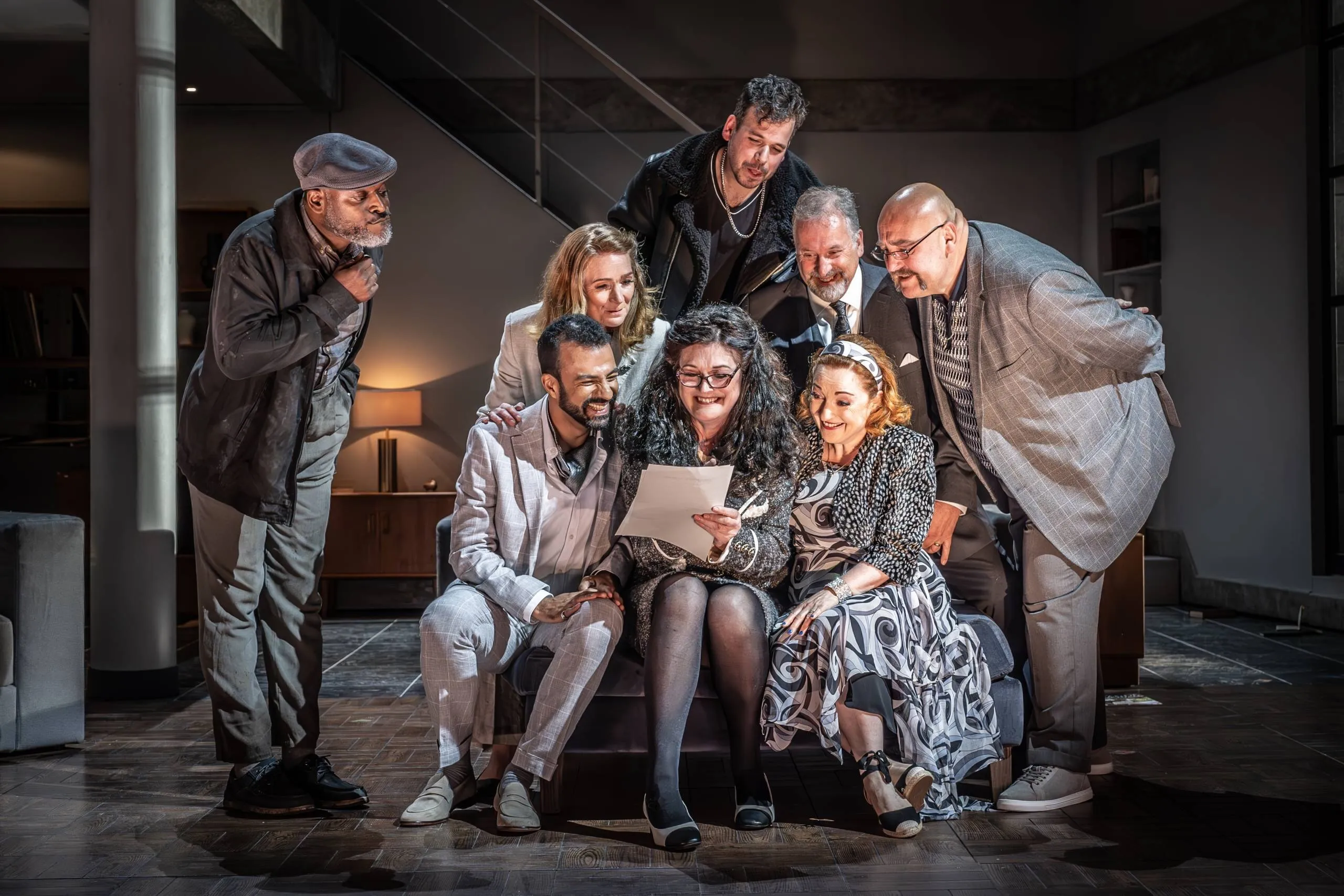 The cast crowds around a sofa reading a letter in a Grange Park Opera production