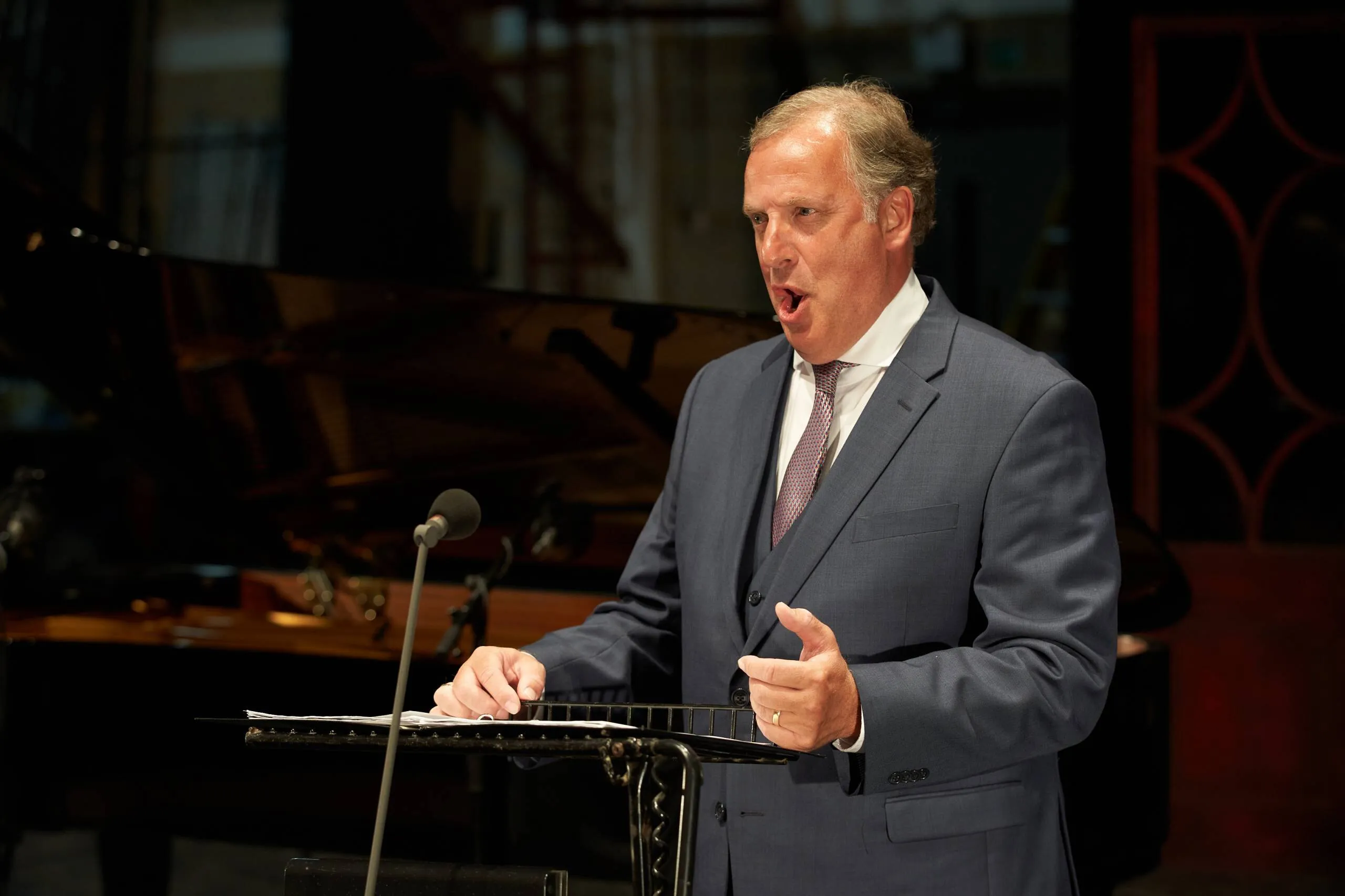 Matthew Brook singing at a music stand in a grey suit
