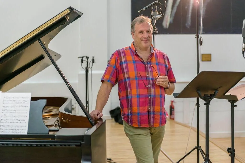 Matthew Brook in a checked shirt, relaxed beside a piano in a rehearsal room