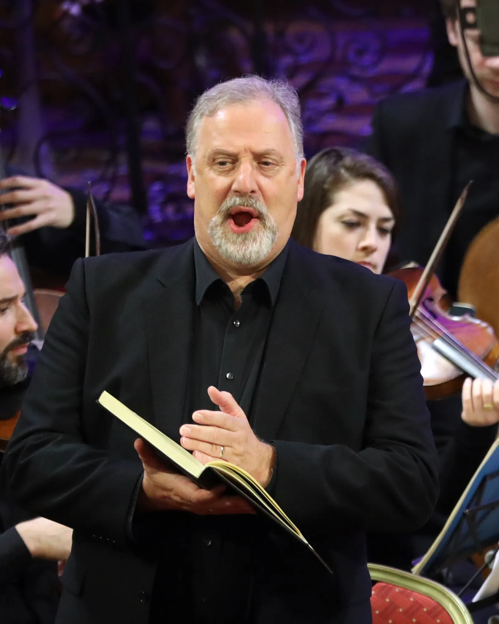 Matthew Brook singing from a score, a violinist of the Irish Baroque Orchestra behind him