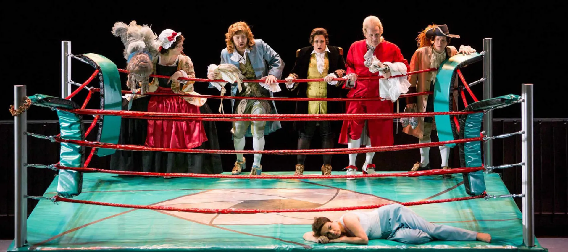 A colourful staged production set in a boxing ring, with the cast on the ropes