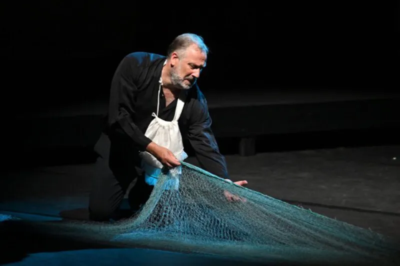 Matthew Brook hauling a fishing net across a dark stage