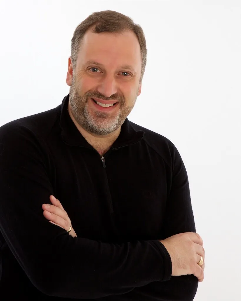 Studio portrait of Matthew Brook, arms folded, against a white background